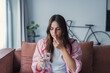 © Daniel - Young woman at home holding a pill and glass of water, looking concerned while considering medication and personal health decisions, illustrating uncertainty, self-care, and everyday healthcare