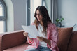 © Daniel - Worried young woman sitting at home reading a paper letter, looking stressed and confused after receiving negative financial news or an unexpected notice, illustrating concern and uncertainty