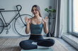 © Daniel - Young woman sitting on yoga mat at home, speaking directly to the camera lens while recording a yoga tutorial, smiling and engaging with viewers in a personal POV perspective