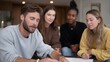 © Bussakon - Diverse group of young adults collaborating and discussing a project around a table indoors