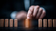 © kaliel - Hand placing a wooden block in a line, symbolizing risk prevention, process control, and strategic business continuity planning.