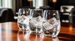 © NoorStudio - Three glasses filled with ice and clear liquid on a wooden table, inviting refreshment.