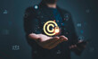 © Dilok - Businessman holding glowing copyright symbol with lock representing intellectual property protection, digital rights management security, online content ownership and legal protection concept.