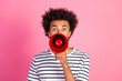 © deagreez - Young African man holding a red megaphone, standing against a pink background wearing a striped t-shirt, expressing enthusiasm