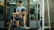 © Prathankarnpap - A woman is performing a kettlebell row on a bench while her trainer closely checks her form
