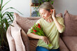 © Tatyana Gladskih - Photo of nice middle age woman looking at flowers tulips bouquet at modern light interior flat indoors, female sitting on sofa at home