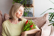© Tatyana Gladskih - Happy woman enjoy bouquet of tulips, sitting on sofa, Housewife enjoying a bunch of flowers of living room