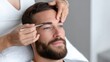 © Ulia_photo - Beautician performing eyebrow grooming procedure on bearded male client in modern beauty salon, close-up crop, trendy men's self-care