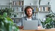 © VictorCanalesStudio - Man wearing headphones focusing on laptop screen in a modern home office with plants
