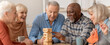 © Prostock-studio - Six seniors are gathered around a table, focused on a game of stacking wooden blocks. They share smiles and laughter while enjoying their time together in a bright indoor space.