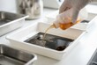 © Stitch - Person pouring brown photographic developer liquid from a bottle into a plastic tray