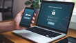 © Stock By Ahmad - Close-up of a person's hand holding a black smartphone displaying a key icon and a 6-digit verification code, next to a silver laptop with a secure login screen and a padlock icon