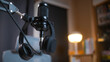 © BJ Day Stock - Close up of empty podcasting workspace with a professional broadcasting microphone and hanging headphones in sharp focus, set against a blurred background of a modern home recording studio.