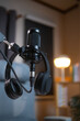 © BJ Day Stock - Close up of empty podcasting workspace with a professional broadcasting microphone and hanging headphones in sharp focus, set against a blurred background of a modern home recording studio.