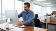 © Mcfarer - Male office worker in blue shirt adjusts computer monitor on wooden desk in modern office with colleagues working in the background