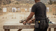 © Mary - Male shooter carefully preparing tactical equipment and firearm magazines on a wooden table at an outdoor gun range.