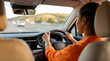 © Esther - Rear view of a focused African American woman confidently driving a modern car on a busy highway during a bright.