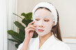 © KMPZZZ - Skin care beauty person concept. Asian young woman applying white cosmetic face mask, sheet pad for treatment moisturizing, relax spa and skin cosmetology. Lifestyle routine therapy of dermatology.