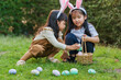 © geargodz - two child girl wearing bunny ears playing together and hunting for Easter eggs into basket on green grass in garden