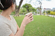 © Jirawatfoto - Contemplative asian woman holding paper cup of coffee relaxing in green park. peaceful moment outdoors with beverage, enjoying beautiful day in garden