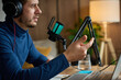 © Lazy_Bear - Man wearing headphones speaks into desktop microphone near laptop at home workspace. Concept of podcasting streaming online communication and content creation