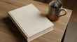 © MuhammadAnns - Blank cream colored hardcover book lying next to a steaming ceramic coffee mug on a light wooden table surface for mockup presentation.