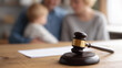 © Tetyana - Gavel on a wooden table with blurred parents and child in background, representing family law, divorce, custody battles, child protection, and adoption legal processes, copy space