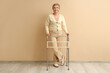© Pixel-Shot - Mature woman with walker near beige wall