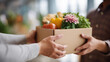 © Denis Yevtekhov - Close-up of faceless volunteer hands distributing a box of food groceries to a recipient at a charity center, defocused charity space behind, food box donation, volunteer giving, charity