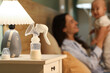 © Pixel-Shot - Breast pump and glowing lamp on table against mother with baby in bedroom at night, closeup