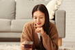 © Pixel-Shot - Beautiful young Asian woman with glass cup of hot tea lying on carpet in living room
