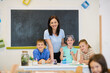 © .shock - Elementary teacher guiding children in a hands-on science experiment in a bright classroom