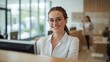 © Future Vision - Smiling receptionist in white blouse and glasses checking guest at reception desk, monitor visible