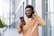 © Liubomir - Young man smiling on an urban street, enjoying music and podcasts on wireless headphones while interacting with his smartphone during a relaxed daily commute