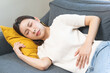 © KMPZZZ - Sick asian young woman in pain, hand holding belly, lying on the sofa with a stomachache, hurt abdomen ache and digestive problem, gastritis or diarrhea. Health care inflammation, abdominal problem