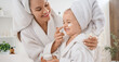 © Pixel-Shot - Cute little happy girl and her mother in bathrobes applying cream at home