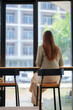 © Tj - Woman sitting by cafe window contemplating city