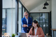 © Tj - Business mentor watching young Asian woman working at laptop