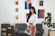 © Studio Marmellata - A professional woman stands in a modern office, holding a tablet and glasses, with abstract art on the wall.