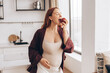 © Maria Vitkovska - Pregnant woman eating red apple in kitchen, healthy pregnancy diet concept