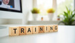 ©  VladaToday - Wooden blocks spelling training on a bright office desk with plants and computer in background for corporate learning and staff development banner