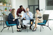 © Dejan - Four multi-ethnic business colleagues having an informal meeting in a modern office lounge, discussing work using a laptop