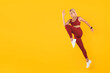 © Prostock-studio - A woman performs an energetic exercise by jumping high in red activewear with a bright yellow background. She focuses on maintaining her form while being active and engaged.