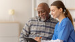 © Prostock-studio - Healthcare worker sits with an older man in a medical office. The worker discusses important information while writing on a clipboard. Both smile and interact in a positive manner.