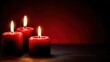© shobakhul - Three burning red candles illuminate a deep maroon and black setting with warm light