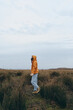 © SHOTPRIME STUDIO - Woman lifestyle concept with a young woman walking outdoors in casual clothes and an orange hoodie. The natural landscape and cloudy sky create a peaceful and reflective mood.