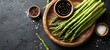 © Wa Bale - Bright asparagus on a wooden plate with seasoning on a dark, textured surface