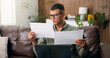 © peopleimages.com - Man, reading and documents with laptop in home for finanial planning, audit or investment on sofa. Male person, checking and paperwork with insurance on computer for budget, finance bills or expenses