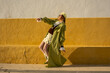© Sunlight - Fashionable woman posing against a bold yellow wall in trendy retro outfit and accessories
