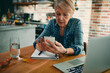 © Davor - Senior woman managing finances on smartphone at kitchen table